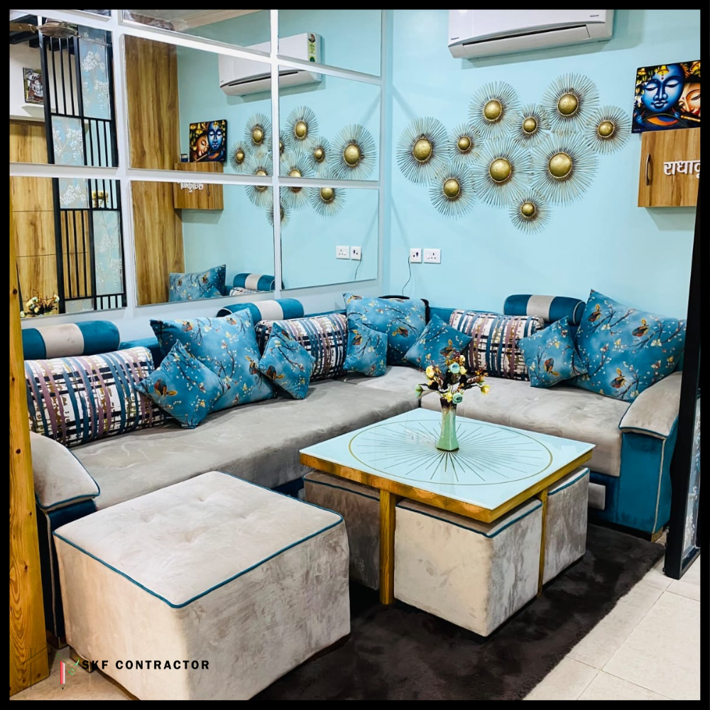 L-shaped grey velvet sofa with teal cushions, matching ottomans, gold sunburst table, and metal wall art.