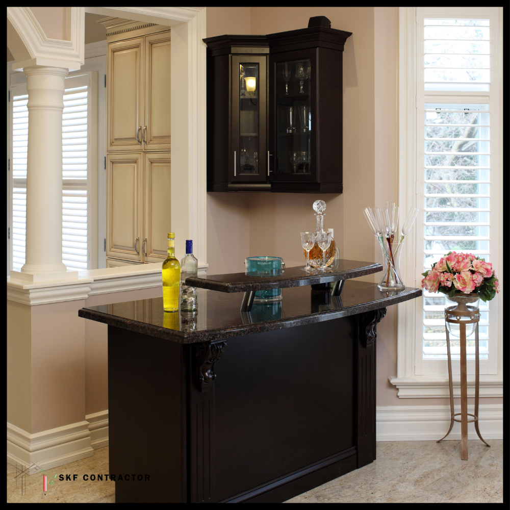 Classic dark wood bar unit with granite top, crystal decanter, lit glass cabinet, and plantation shutters.