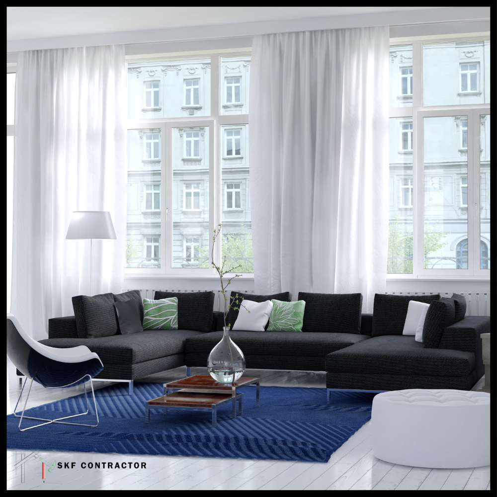 Dark grey L-shaped sofa set with green cushions, blue rug, glass vase centrepiece, and sheer floor windows.