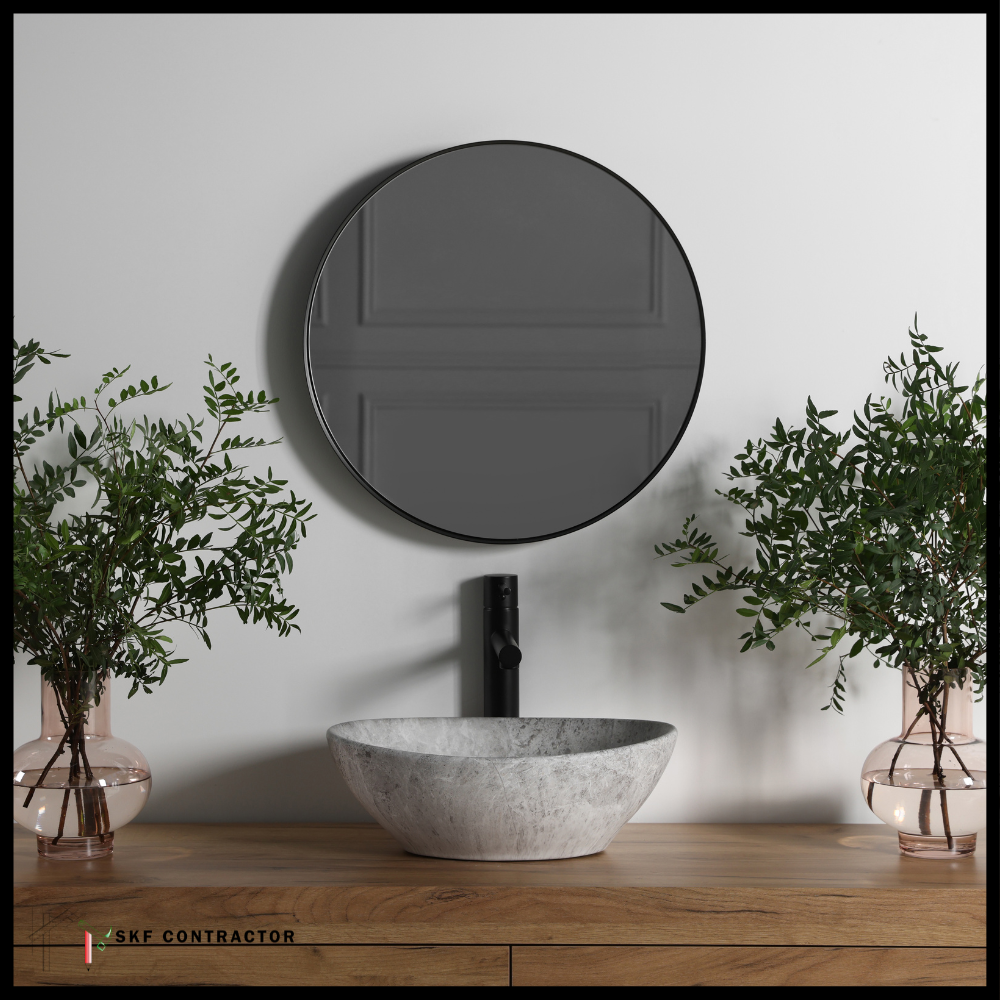 Grey marble vessel sink, matte black faucet, round black mirror, oak vanity top, and green botanical vases.
