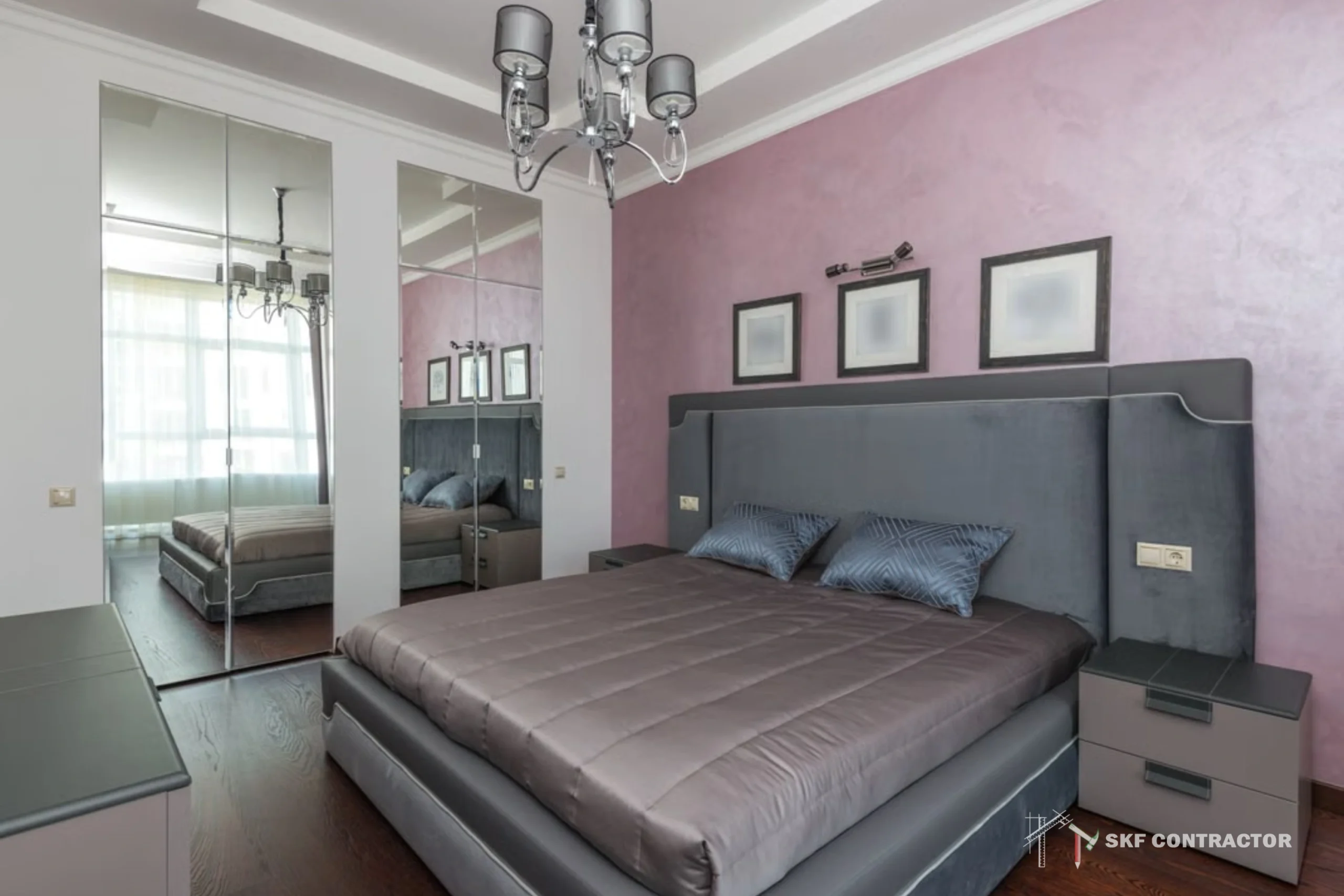 Modern bedroom with a gray upholstered bed, mauve accent wall, chandelier, mirrored wardrobe, framed art, and a calm luxury feel.