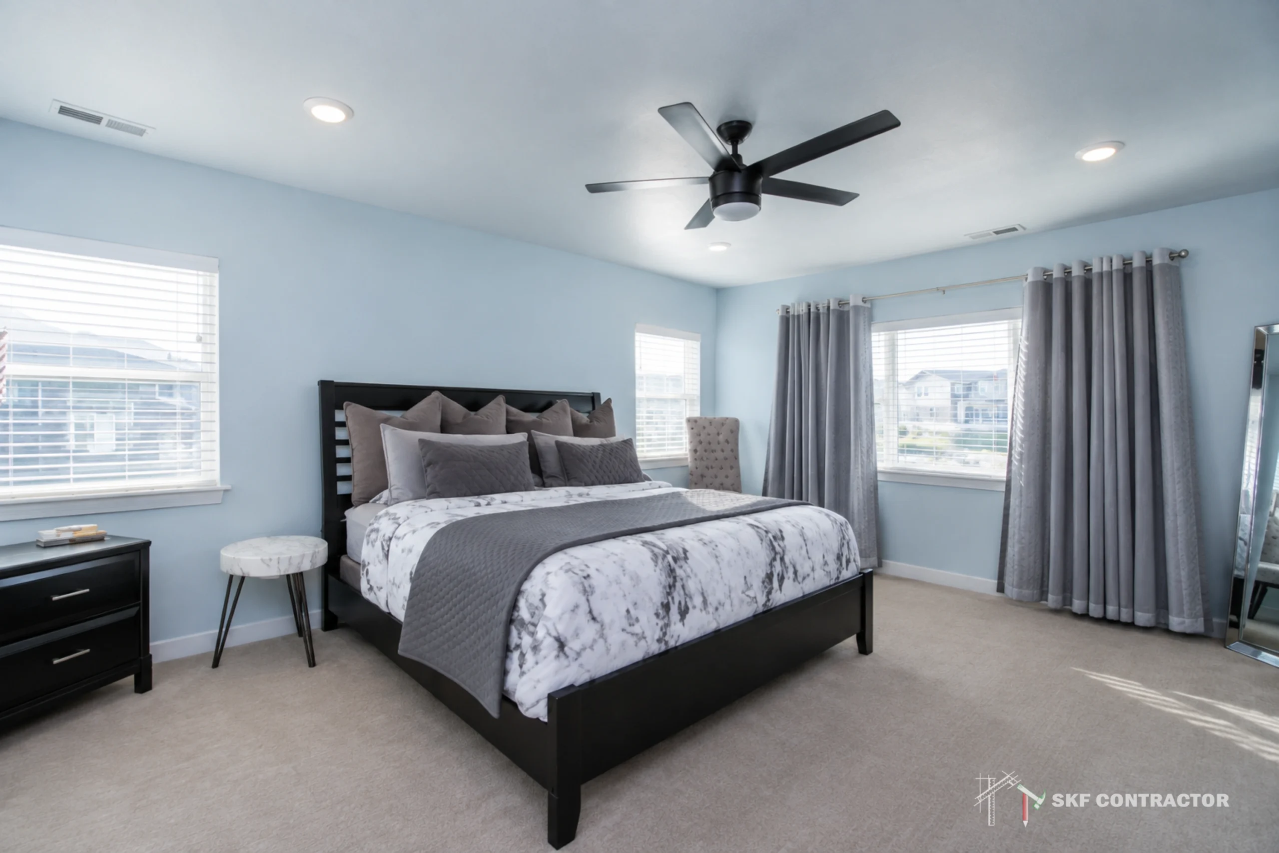 Bright, serene modern bedroom with a marble-patterned bed, gray curtains, blue walls, ceiling fan, and abundant natural daylight.