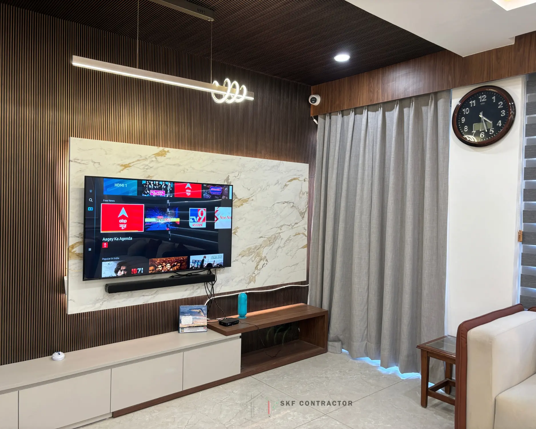Living room TV wall with wooden slat panelling, marble back panel, floating TV unit and LED lighting by SKF Contractor, Delhi